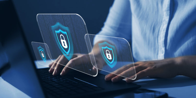 person sitting at laptop with hands on the keyboard, images of a white lock inside a blue crest over top of her hands