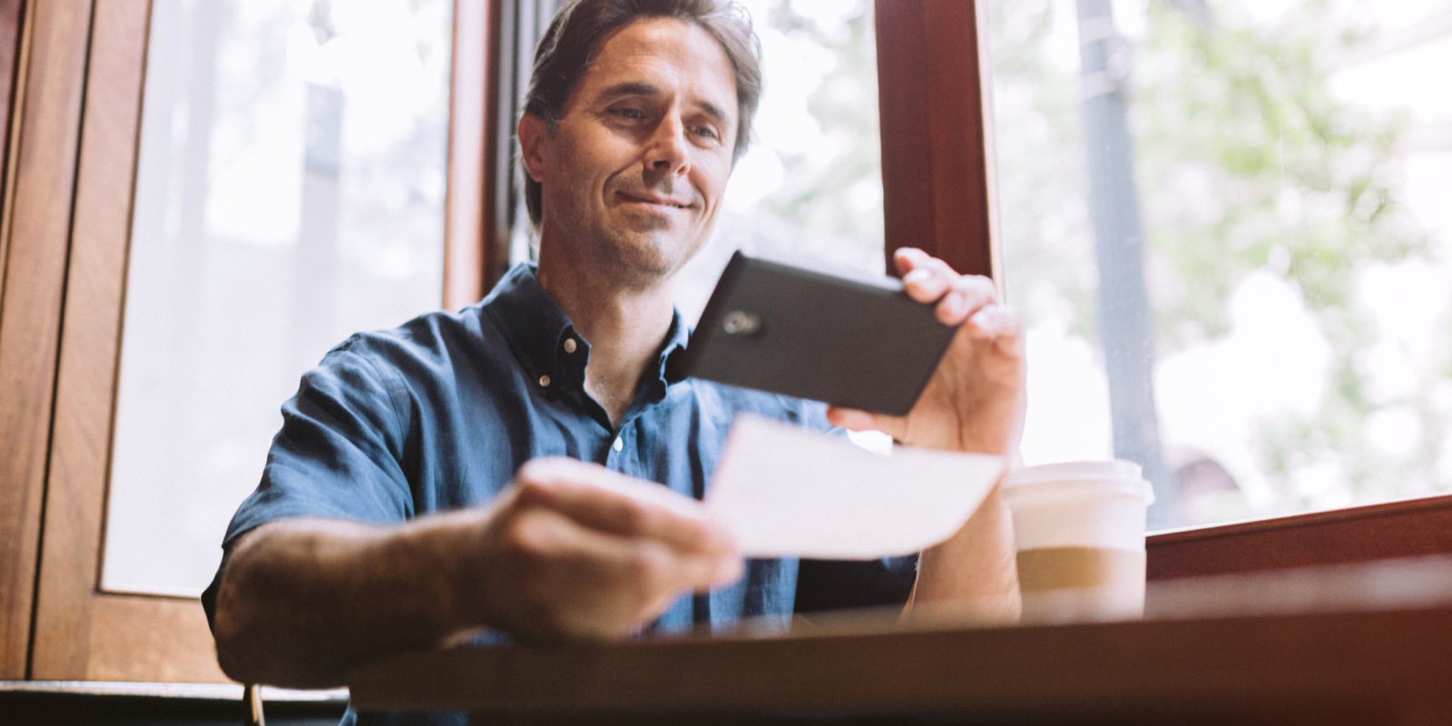 man in a blue button down shirt takes a photo of a check with his smart phone