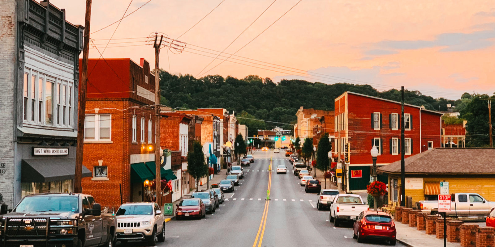 A quiet city street at twilight, lined with cars on either side, brick buildings, and with powerlines overhead