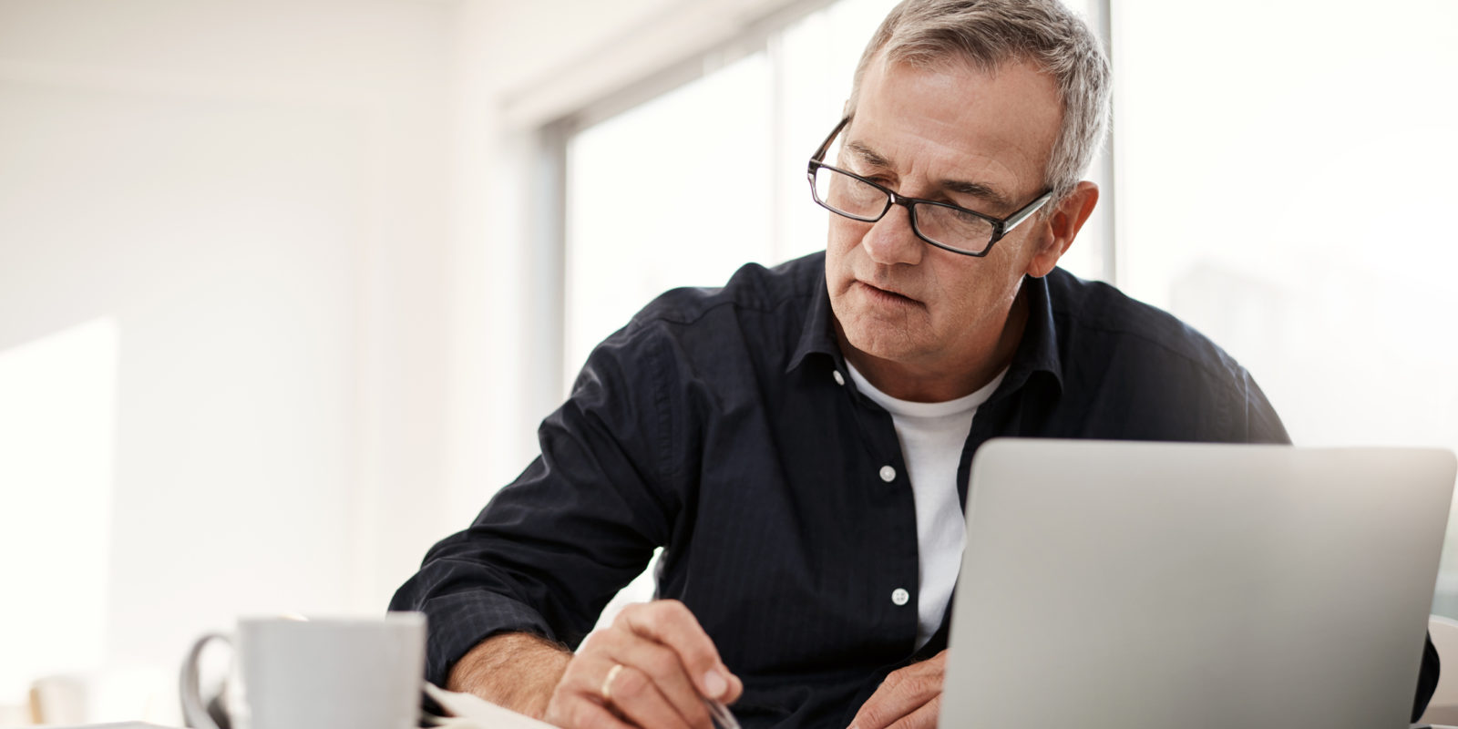man in black button down and glasses sits at computer and holds a pen