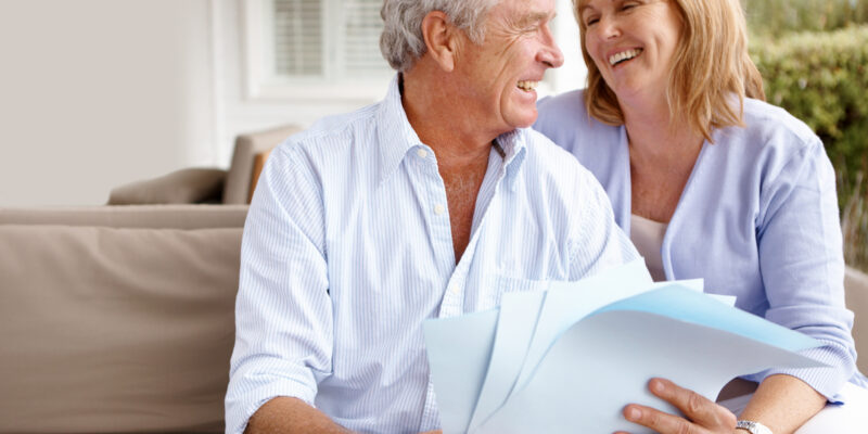Older man holding papers and woman sit on a couch and laugh